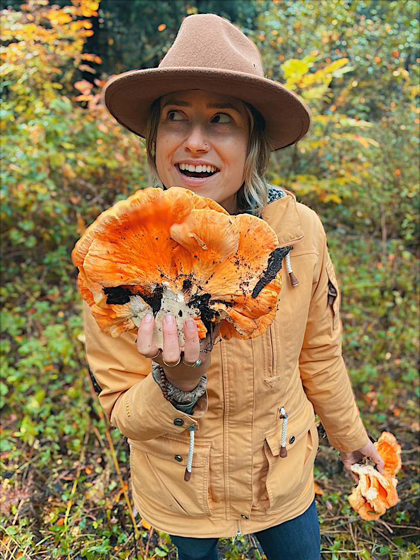 Wild & Well's founder standing in autumn woodland, holding a large bracket of chicken-of-the-woods mushroom