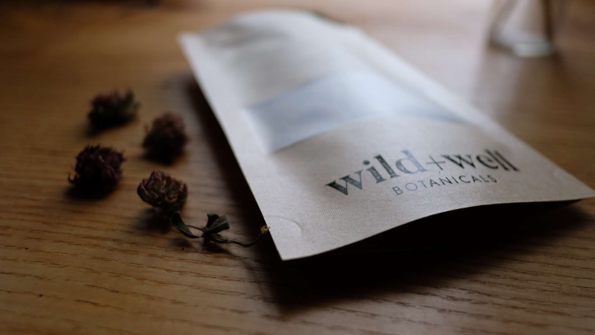 Close-up of a kraft paper pouch resting beside dried clover, shot low with a soft background